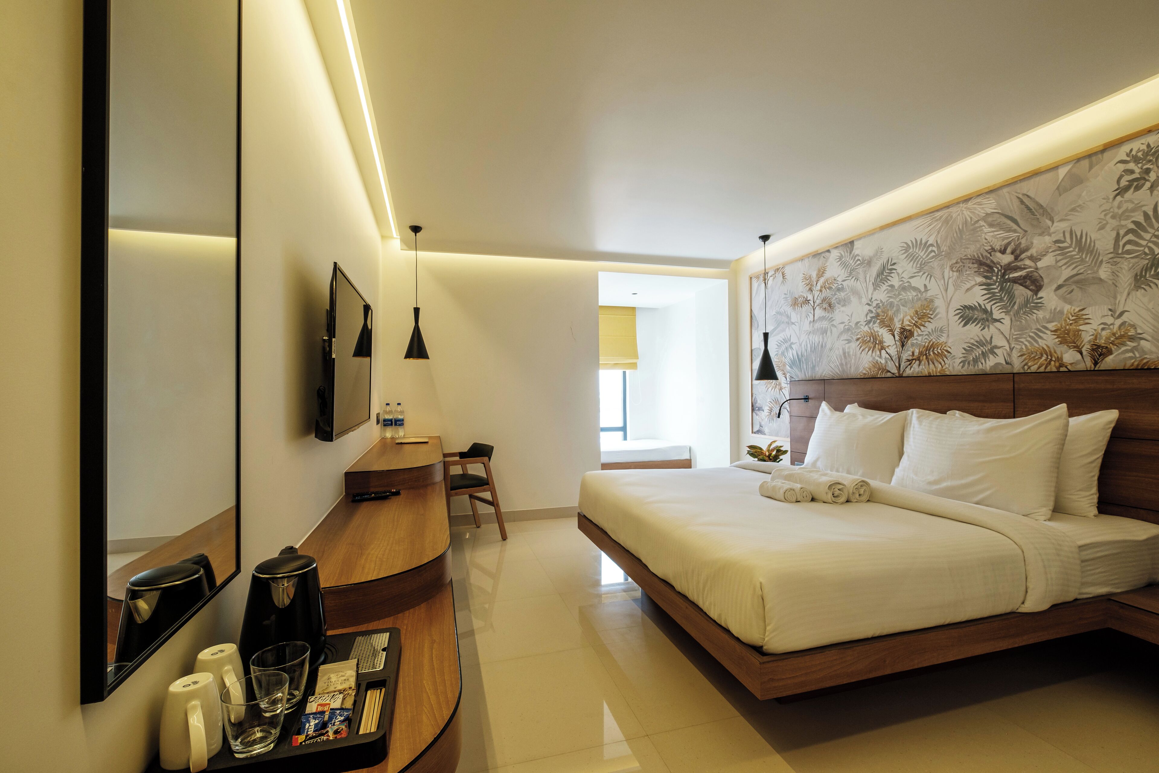 A modern hotel room with a large bed, a desk with a coffee maker, and a mirror.