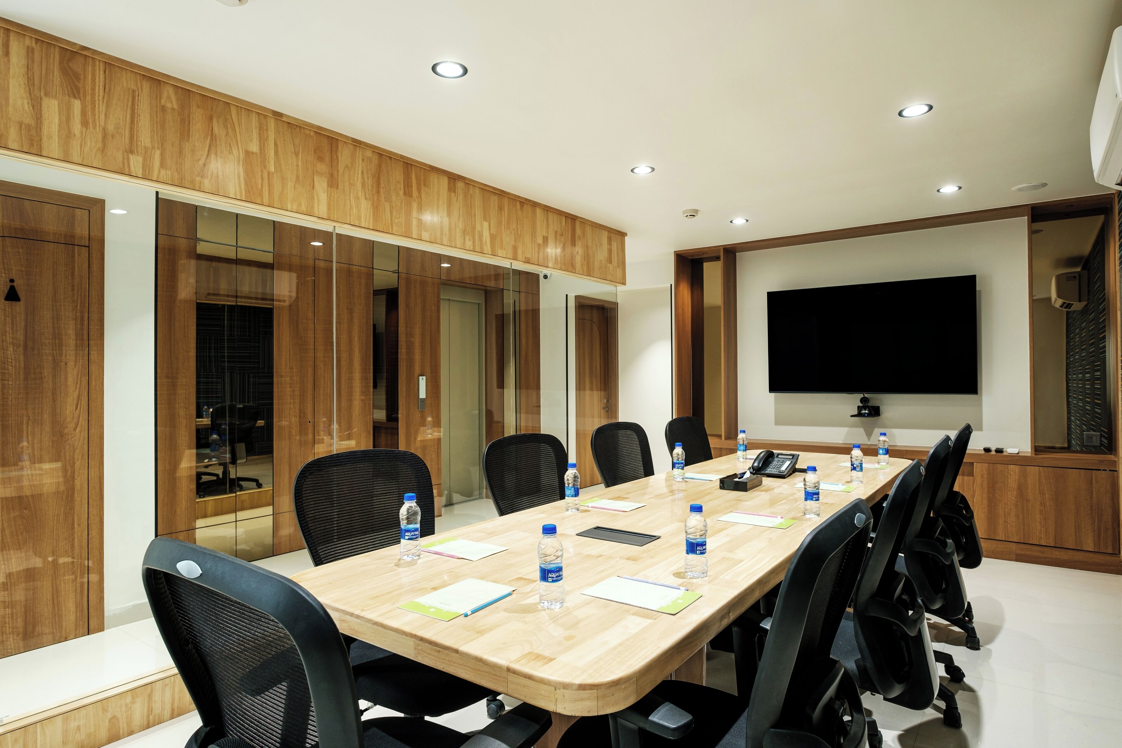 A conference room with a long table, black chairs, and a large screen.
