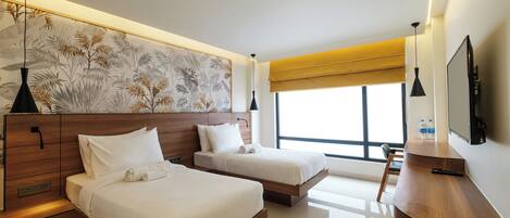 Quarto de hotel moderno com duas camas, uma escrivaninha de madeira, uma janela grande e uma televisão fixada na parede.