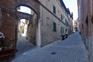 Una calle estrecha con un arco de ladrillo, motocicletas estacionadas y una hilera de edificios con contraventanas.