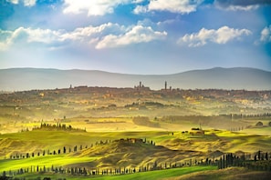 Vista panorámica de un paisaje montañoso con un pueblo a lo lejos, que muestra campos verdes ondulantes y una iglesia destacada.