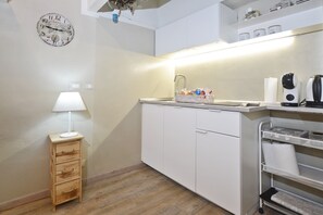 A kitchenette with a sink, a clock, a small wooden cabinet, and a shelf with kitchen items. - Casina Di Giada (Siena)