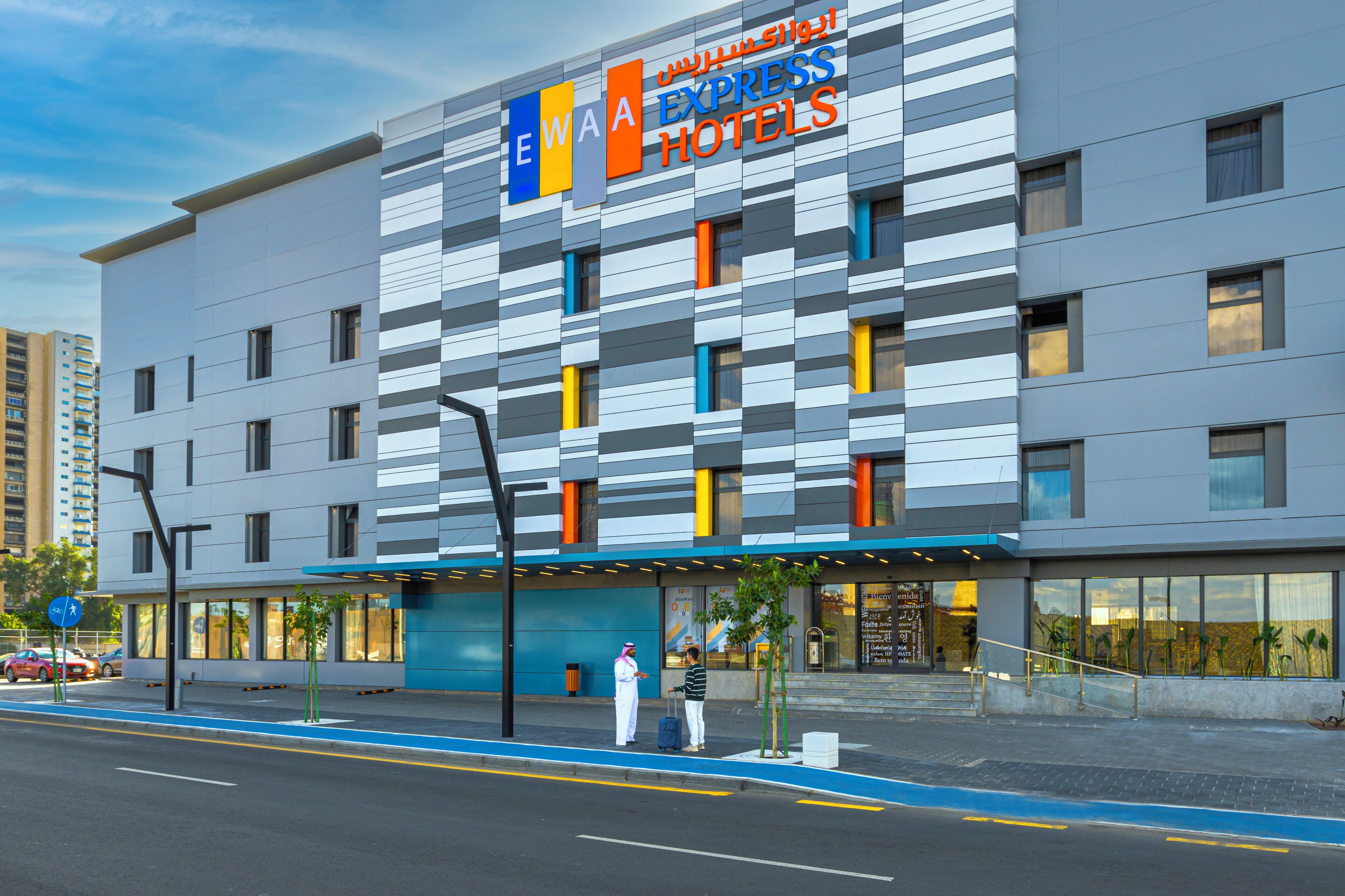 A modern hotel with a blue and white facade, multiple floors, and a sign indicating it is an EWA hotel.
