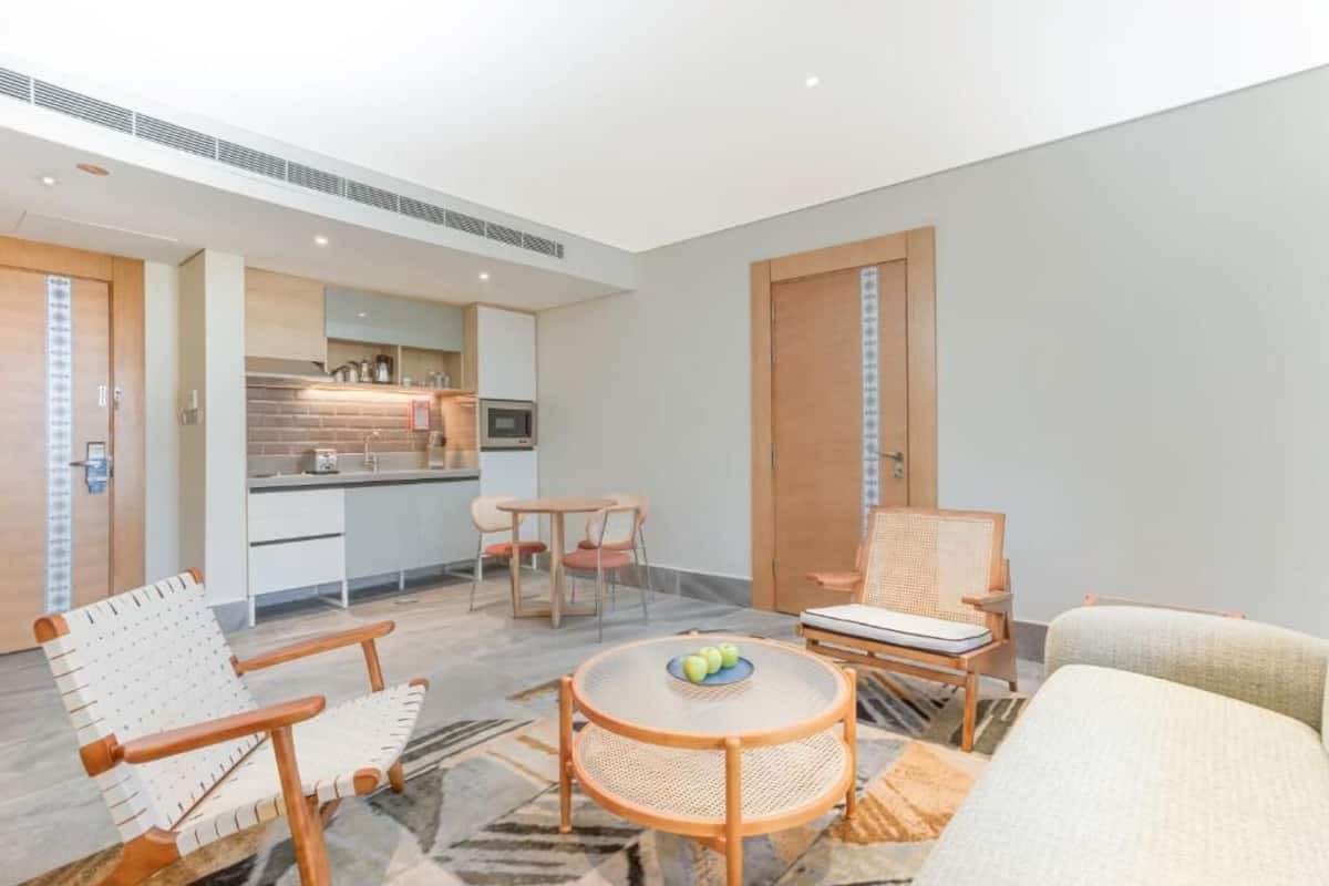 A modern living room with a round coffee table, two chairs, a sofa, and a kitchen area in the background.