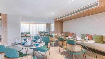Uma sala de jantar de hotel moderna, com mesas redondas, cadeiras cor turquesa e um sofá com almofadas.