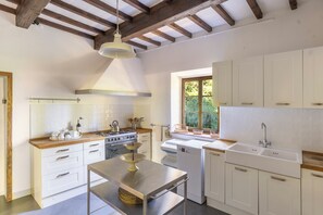 Una cocina moderna con armarios blancos, una mesa de acero inoxidable y un ventanal que proporciona luz natural.