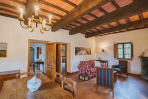 Ein Essbereich mit einem Holztisch, Stühlen und einer Chandelier. Ein Sofa und ein Fenster mit Blick auf Bäume sind ebenfalls vorhanden.