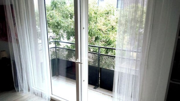 Una habitación con un gran ventanal corredero que da a un balcón con baranda metálica.