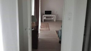 Un pasillo con una puerta blanca, un televisor sobre un mueble bajo y una alfombra en el suelo.