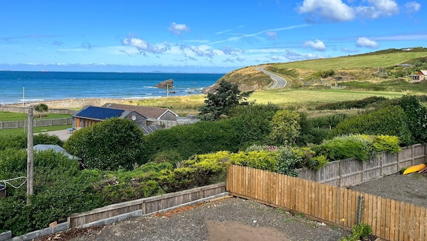 A coastal landscape with a winding road, a wooden fence, and a view of the sea.