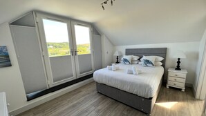 A bedroom with a bed, bedside tables, a window, and a view of greenery.