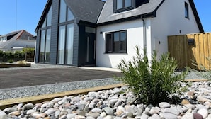 A modern two-story house with a sloped roof, large windows, and a gravel driveway.