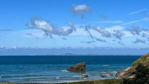 A coastal landscape with clear skies, a large rock formation, and calm sea.