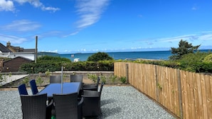 An outdoor patio with a table and chairs, a wooden fence, and a view of the sea.