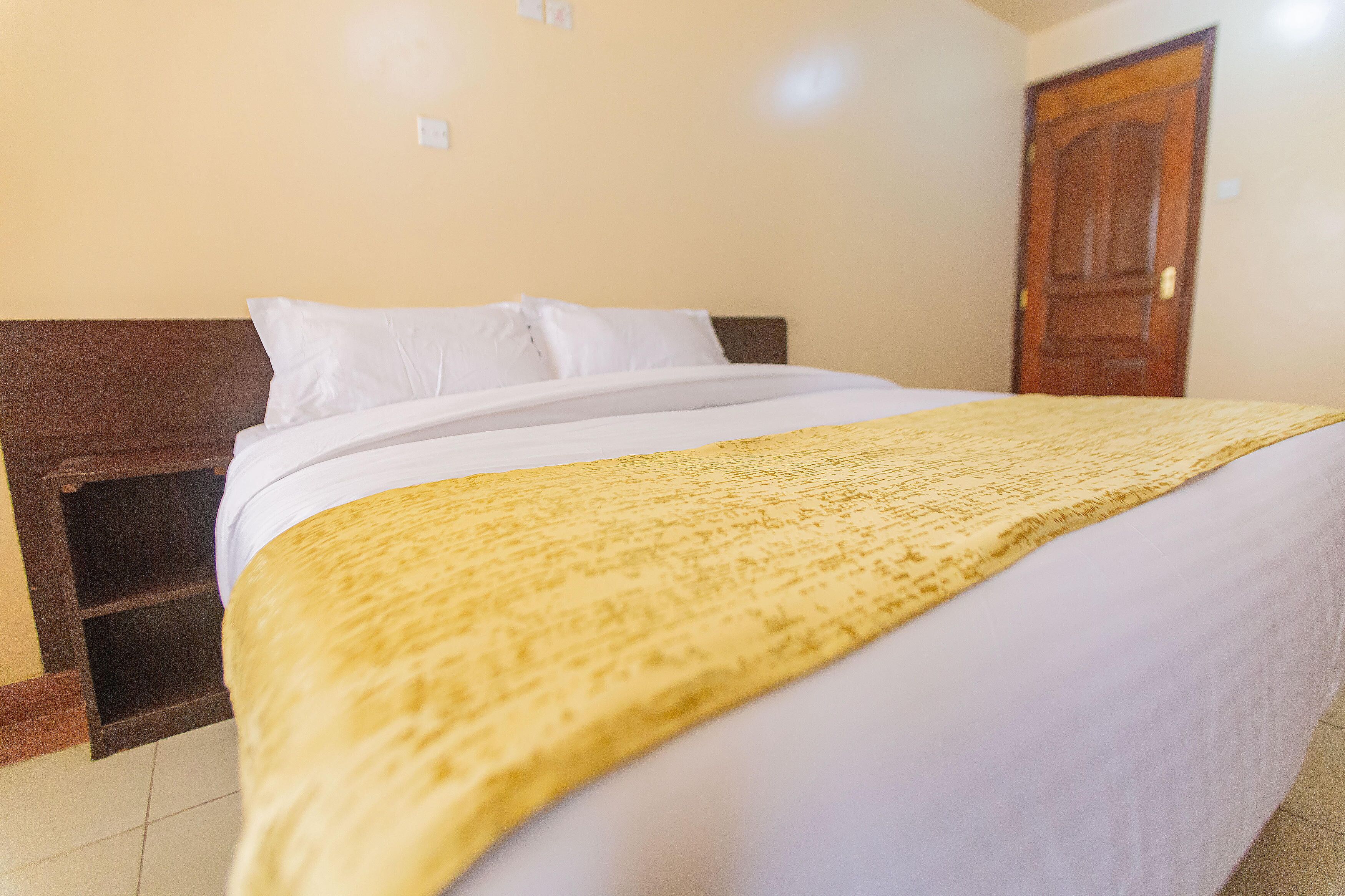 A bed with a white mattress and a yellow blanket, a wooden headboard, and a wooden door in the background.