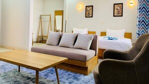 A modern hotel room with a sofa, a bed, a chair, and a wooden table. - Canwin Hotel (Accra)