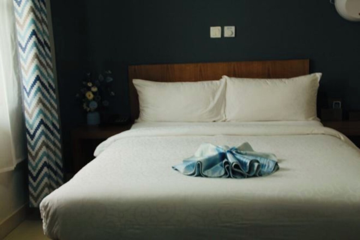 A neatly made bed with white linens and a blue towel on the bed.