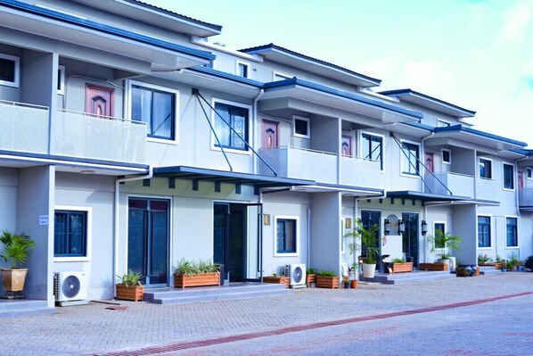 Un hotel moderno de varios pisos con balcones, unidades de aire acondicionado y plantas en macetas.
