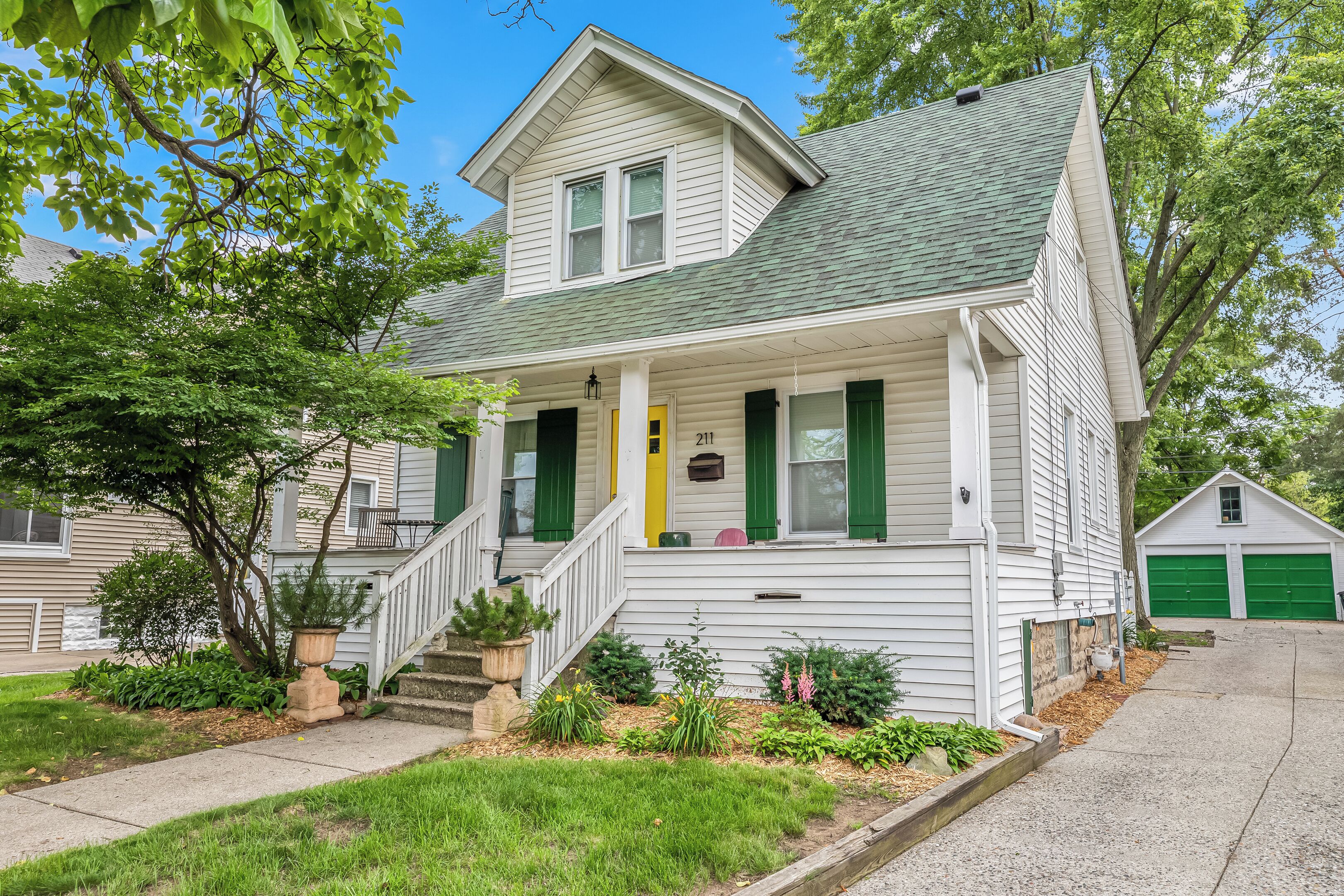 A two-story house with a front porch, green shutters, and a garage.