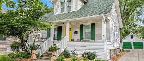 A two-story house with a front porch, green shutters, and a garage.
