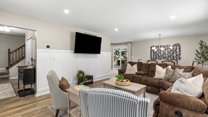 A spacious living room with a large brown sectional sofa, a flat-screen TV mounted on the wall, and a decorative wall piece. - Modern [3BR/2BA] Family Home in Commerce Township (Commerce Township)