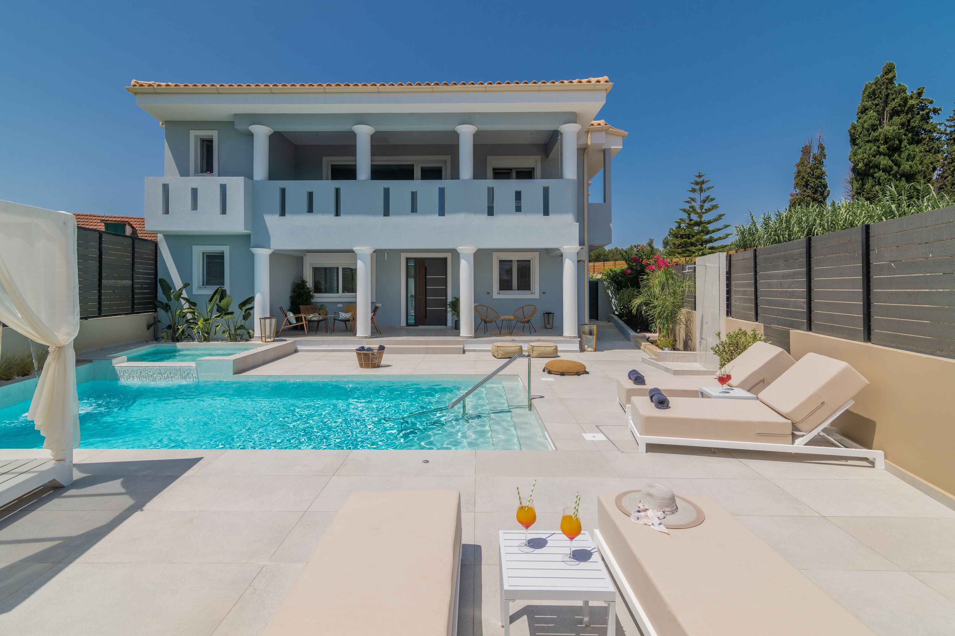 A two-story building with a swimming pool, outdoor seating, and a garden.