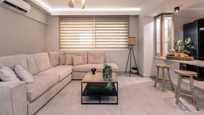 A modern living room with a beige sofa, a wooden coffee table, and a large window with blinds. - Fratelli Villa, with Heated Pool & Spa Whirlpool  (Zakynthos)