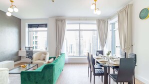 Een moderne woonkamer met een groene bank, een eettafel voor vier personen en een groot raam met gordijnen.