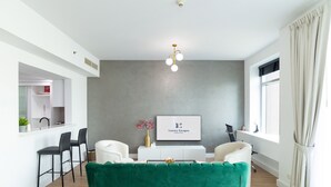 Een moderne woonkamer met een groene bank, witte stoelen, een salontafel en een ingelijst schilderij aan de muur.