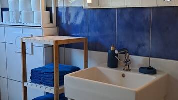 Bathroom features a sink, mirror, and shelf with towels.