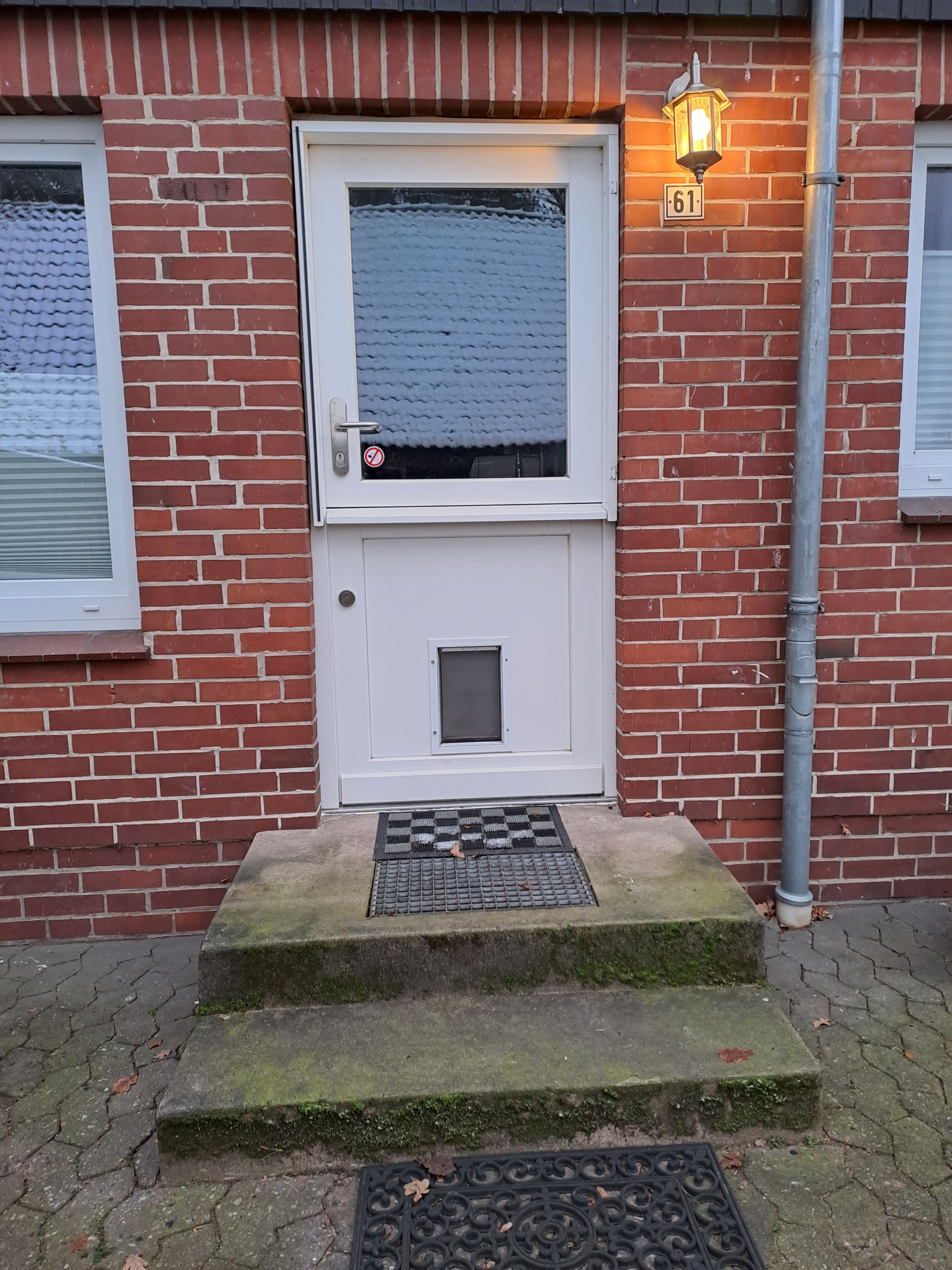 A red brick building with a white door, a small window, and a number '61' sign.