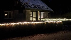Una casa con techo nevado, ventanas iluminadas y un sendero que la conduce.