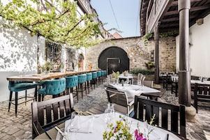 Un espacio de comedor al aire libre con varias mesas y sillas, un muro de piedra y un arco de madera.
