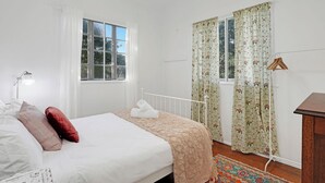 Un dormitorio con cama, lámpara de noche, ventana con cortinas y una alfombra estampada.