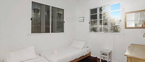 A room with two beds, a small table, a ceiling fan, and a window with a view of trees.
