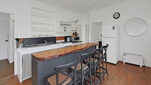 Una cocina moderna con armarios blancos, una barra de madera y una zona de estar con sillas de metal.