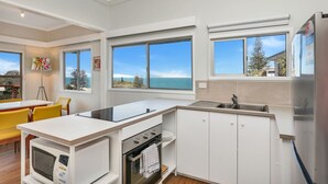 A modern kitchen with white cabinetry, a built-in oven, a microwave, and a large window overlooking a scenic view. - One bedroom cottage - Ideal couples retreat (Point Lookout)