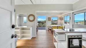 A modern kitchen with white cabinetry, a built-in oven, and a dining area with yellow chairs. - One bedroom cottage - Ideal couples retreat (Point Lookout)
