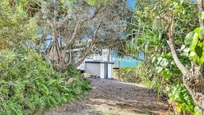 A dirt path leading to a small white building with a blue roof, surrounded by dense vegetation and trees. - One bedroom cottage - Ideal couples retreat (Point Lookout)