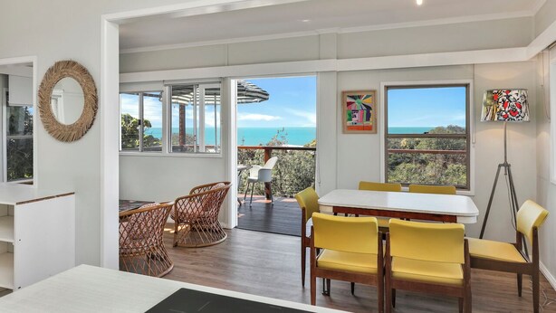A spacious room with a large dining table, yellow chairs, wicker chairs, and a view of the ocean. - One bedroom cottage - Ideal couples retreat (Point Lookout)