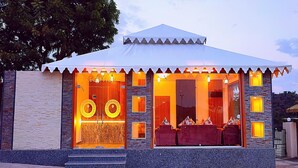 A modern building with a covered entrance, large windows, and a stone facade. - The Sky Imperial  Nakoda Green Valley  (Nathdwara)