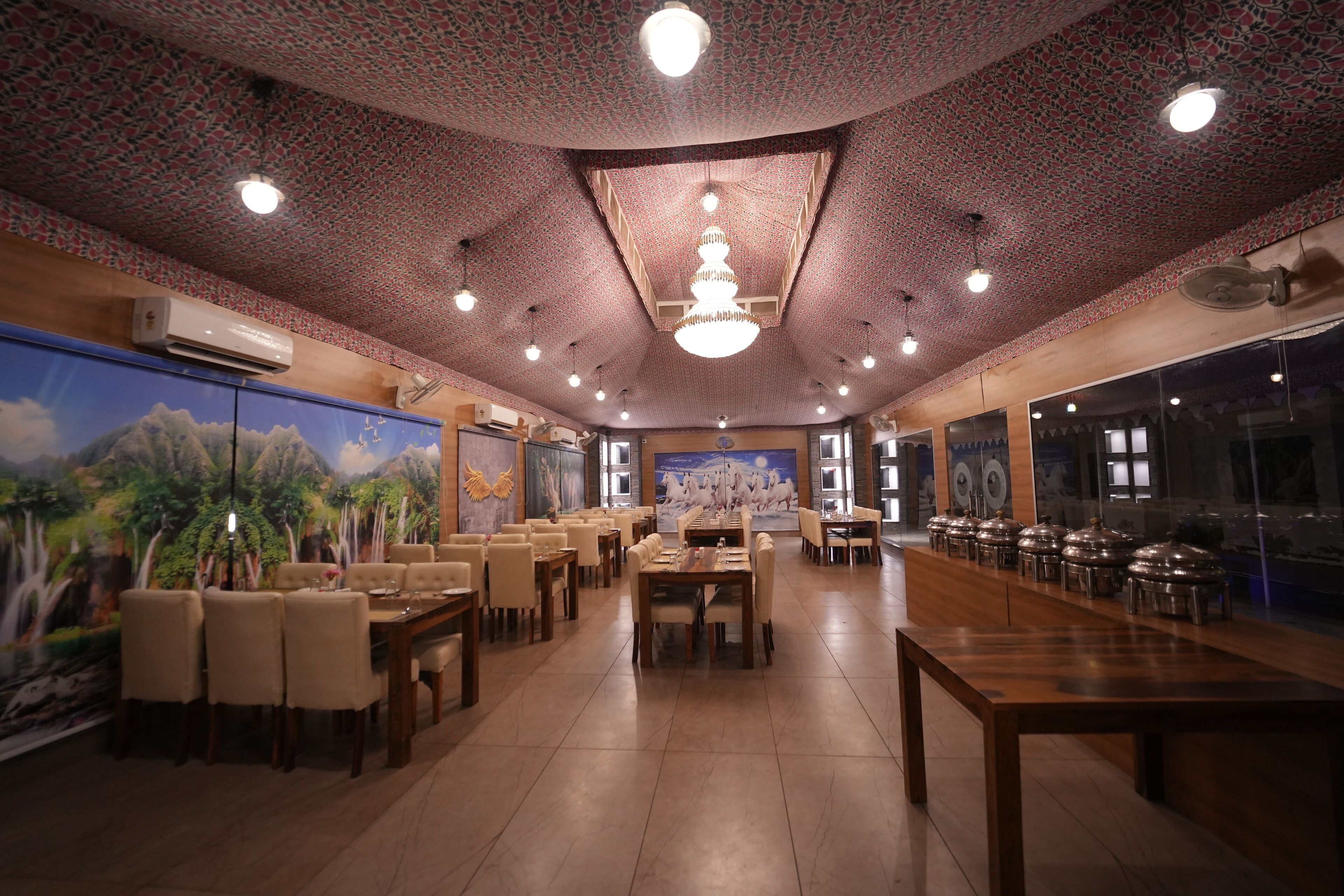 A restaurant with a high ceiling, patterned ceiling, and chandeliers. Tables and chairs are arranged for dining.