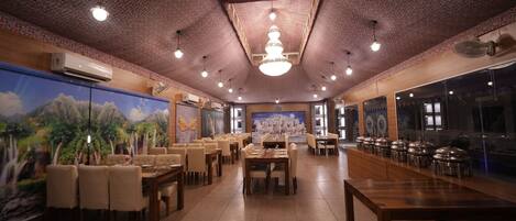 A restaurant with a high ceiling, patterned ceiling, and chandeliers. Tables and chairs are arranged for dining.