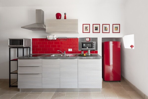 A modern kitchen with a grey countertop, red backsplash, and a red refrigerator.