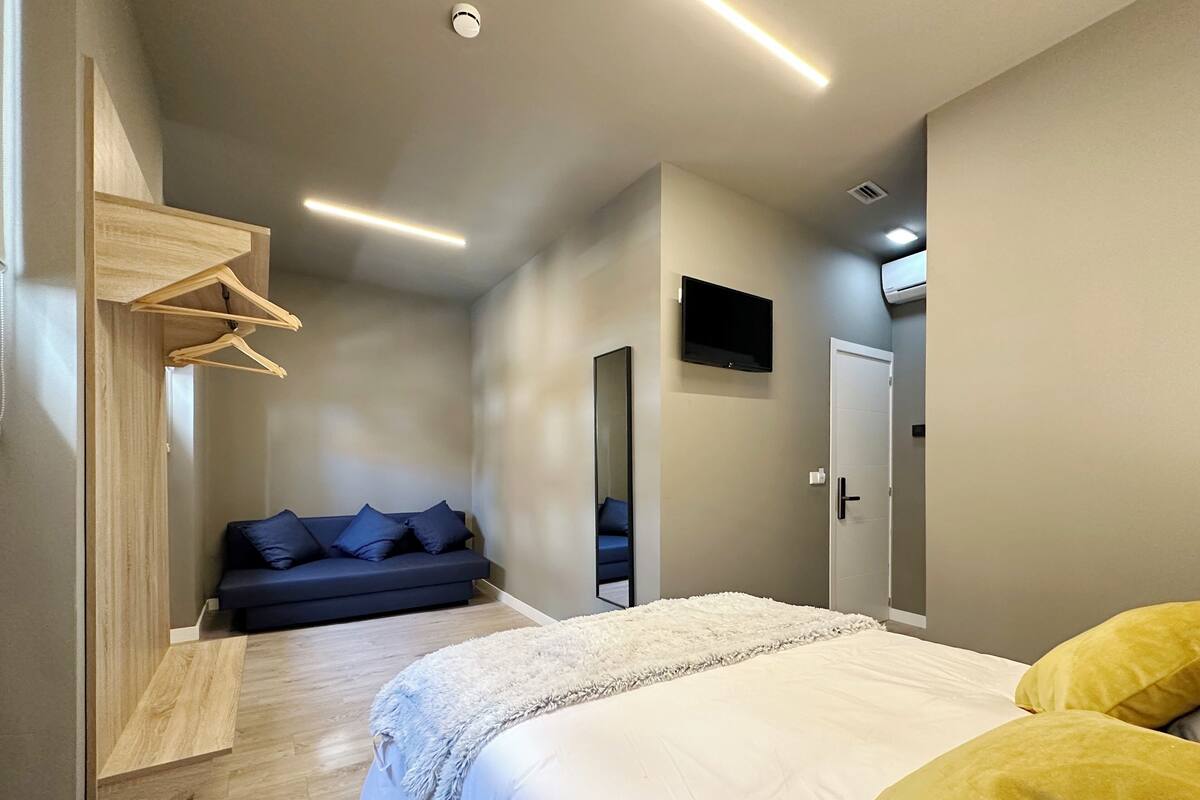 A modern bedroom with a bed, a sofa, a TV, and a wardrobe.