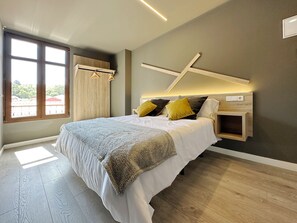 A modern bedroom with a large bed, wooden headboard, and a view of the outdoors through a window. - Hostal María Felisa (Carreno)