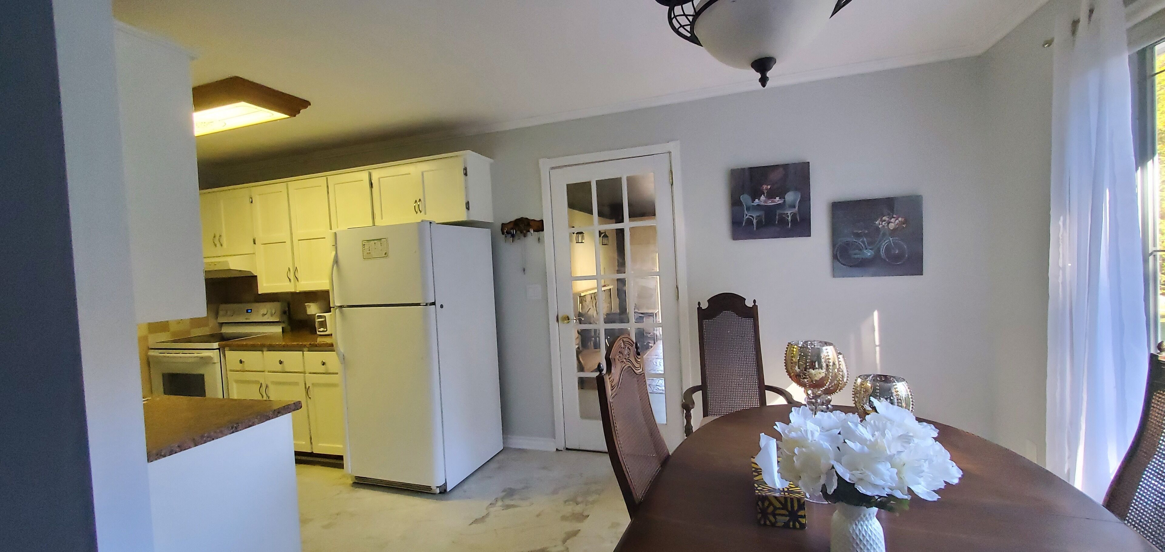 A kitchen with white cabinets, a refrigerator, and a dining area with a table set for two.