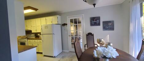 A kitchen with white cabinets, a refrigerator, and a dining area with a table set for two.