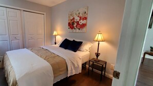 Um quarto com uma cama, duas luminárias de cabeceira, um quadro na parede e uma porta.
