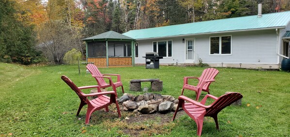 A house with a screened porch, a fire pit, and four Adirondack chairs in the yard.